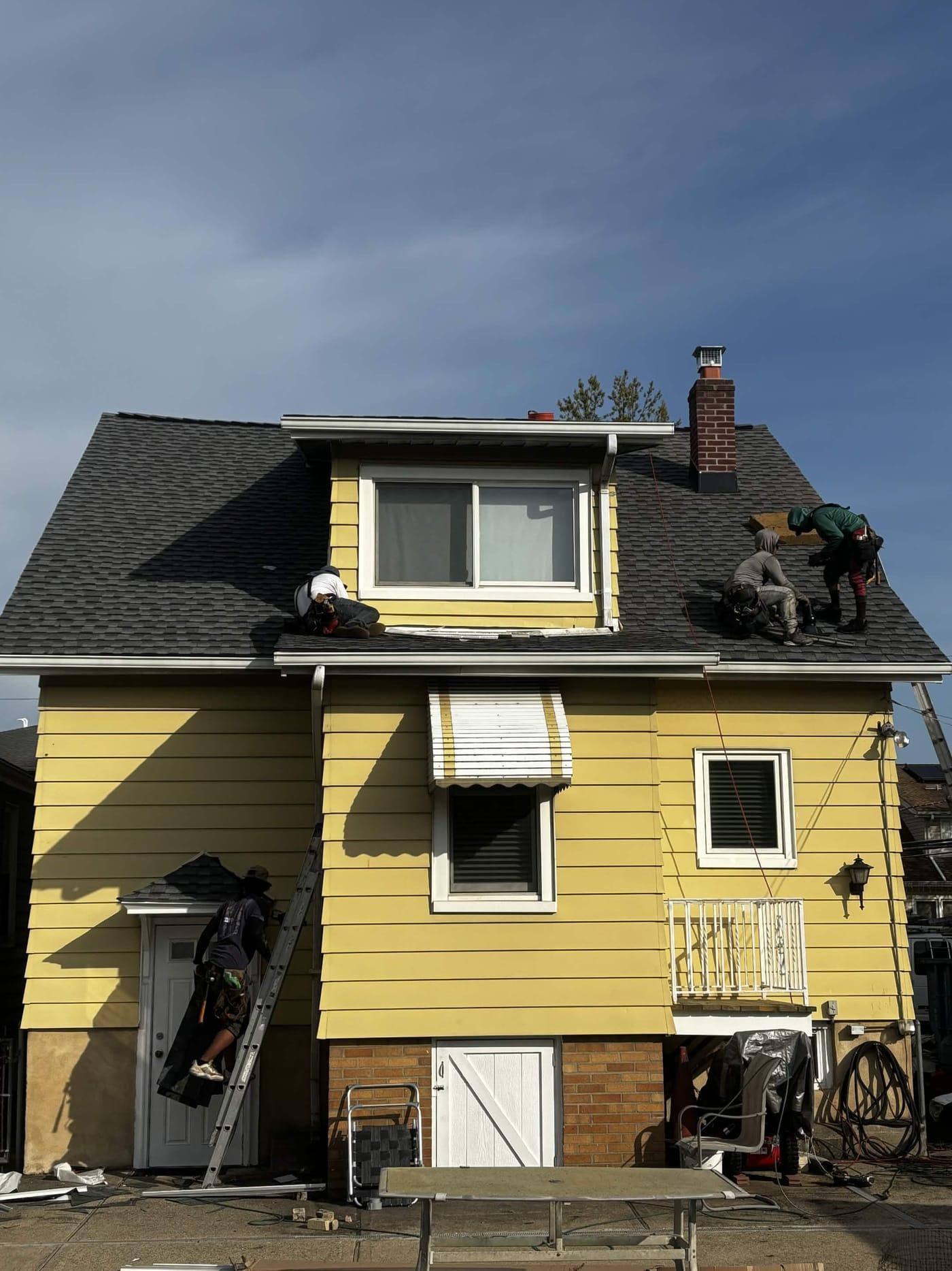 Four Elevate HRG crew members working a roof replacement on a New Jersey home, one climbing a ladder to the eave