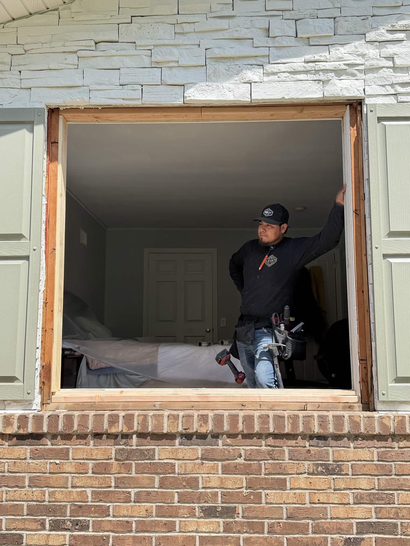Elevate HRG installer standing in an open window frame, furniture inside covered with protective sheeting
