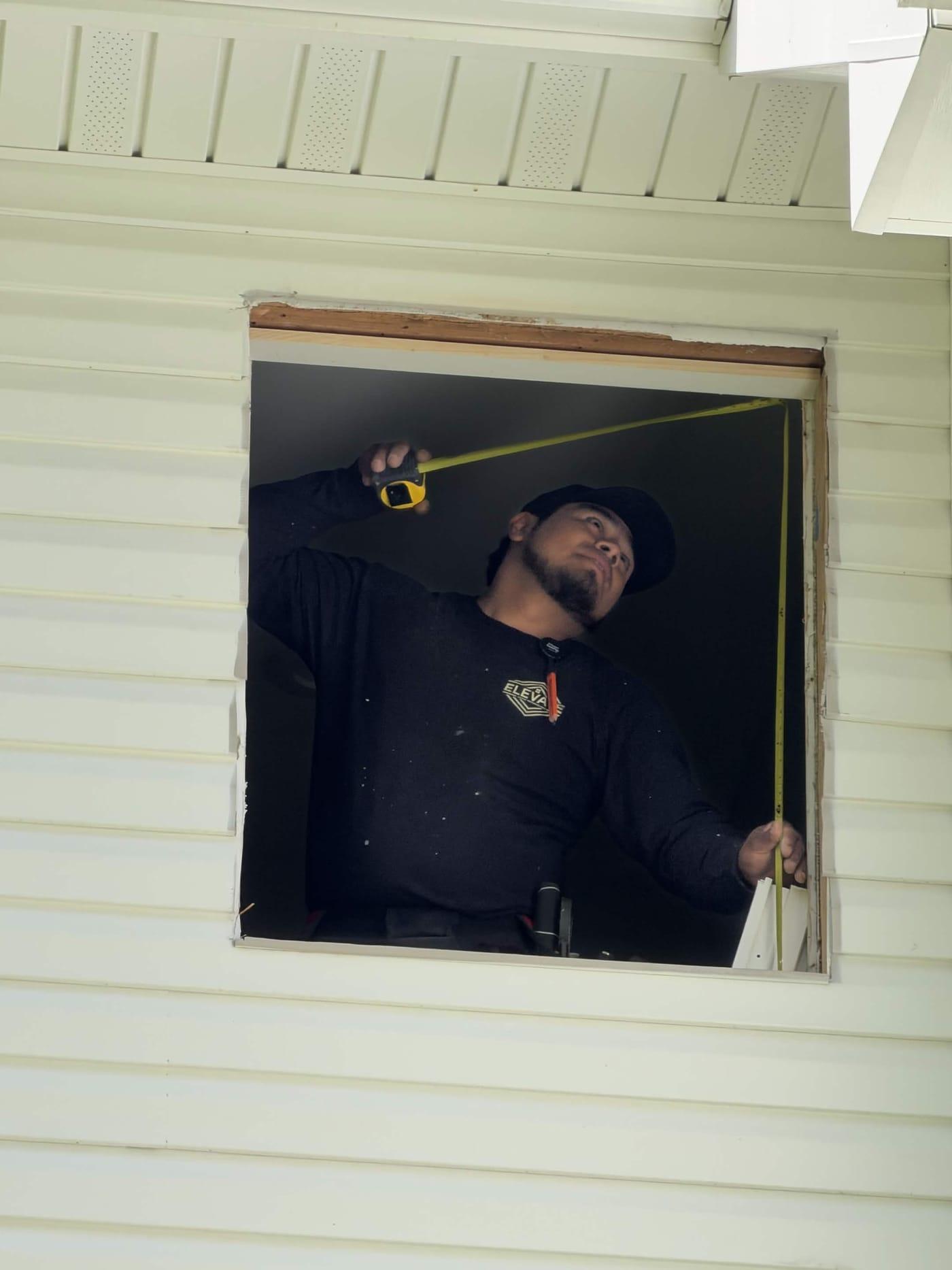 Elevate HRG installer measuring a window rough opening with a tape measure