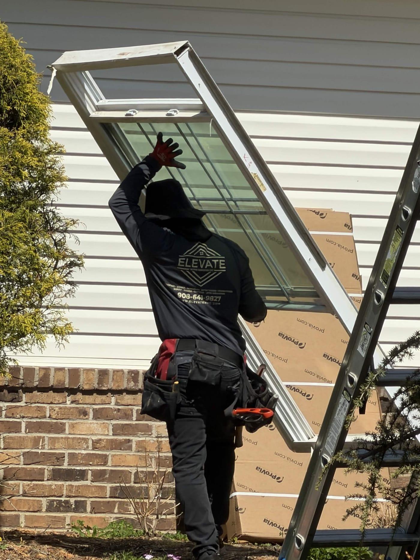 Elevate HRG installer lifting an old window sash out of its opening, ProVia cartons stacked behind